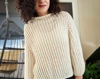 May include: A white knitted sweater with a loose fit and a ribbed texture. The sweater has long sleeves and a round neckline.