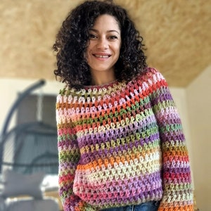 May include: A multi-colored crochet top with a striped pattern in shades of pink, purple, orange, green, and white. The top has long sleeves and a loose fit.