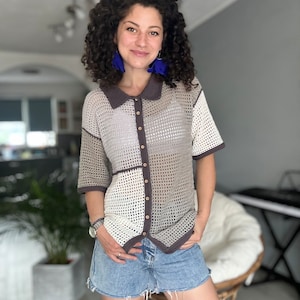 Könnte beinhalten: Eine Frau trägt ein braunes und weißes Häkeltop mit Kragen und Knopfleiste. Das Top hat ein geometrisches Muster und ist halbtransparent. Sie trägt auch blaue Jeans-Shorts.