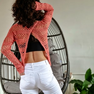 May include: A woman wearing a coral crochet top with a criss-cross back design and white jeans.