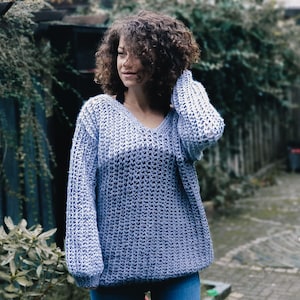 Puede incluir: Un suéter de punto azul claro con cuello en V y mangas largas. El suéter está hecho de un tejido de punto suelto y tiene un ajuste holgado.