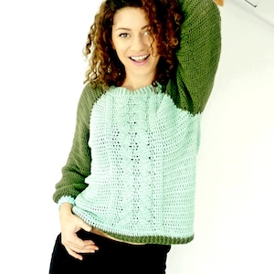 May include: A green and light green crocheted sweater with a cable knit pattern. The sweater has long sleeves and a round neckline.