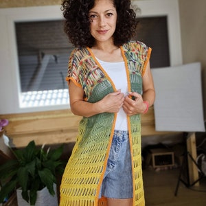 May include: A long, crocheted vest with a gradient of yellow, green, and orange. The vest has a loose fit and a sleeveless design. It is made with a delicate crochet stitch and has a fringed hem.
