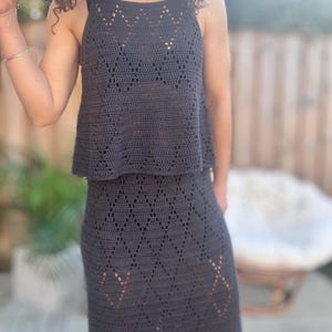 Pode incluir: Um conjunto de top e saia de crochê cinza escuro. O top é estilo regata com decote quadrado. A saia é longa, com um padrão de diamante. O conjunto é feito de um material macio e respirável.