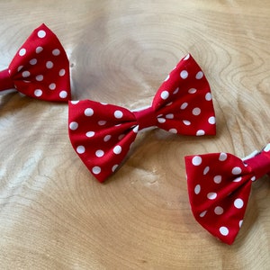 May include: Three red bow ties with white polka dots. The bow ties are made of fabric and have a simple design.