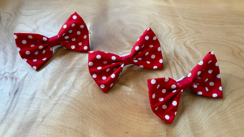 May include: Three red bow ties with white polka dots. The bow ties are made of fabric and have a simple design.