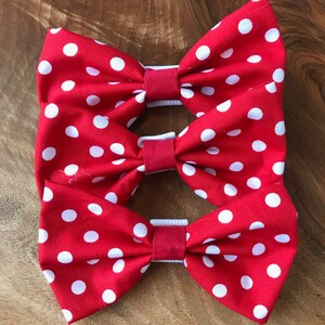 May include: Three red fabric bow ties with white polka dots. The bow ties are stacked on top of each other.
