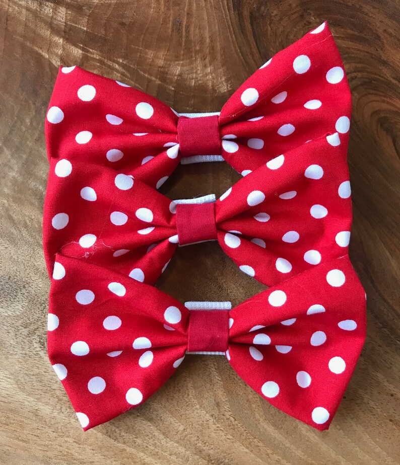 May include: Three red fabric bow ties with white polka dots. The bow ties are stacked on top of each other.