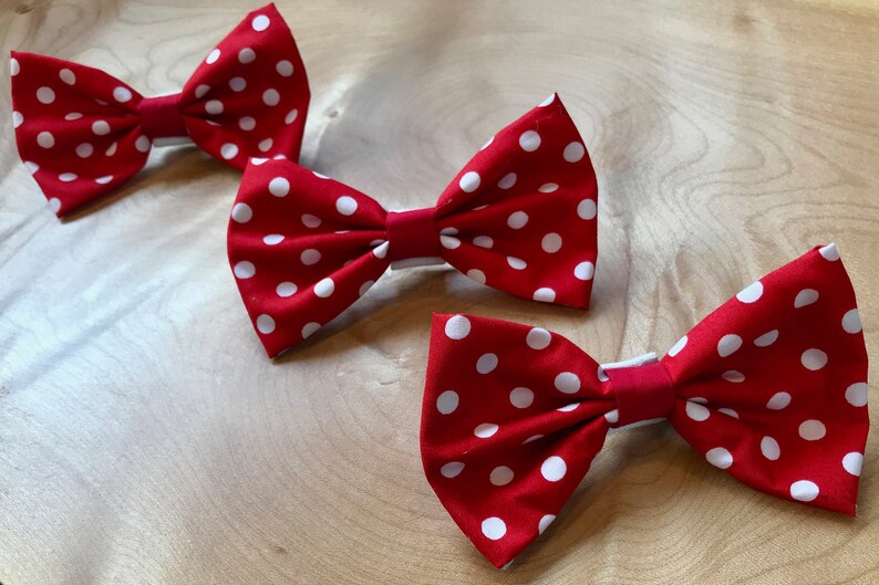 May include: Three red bow ties with white polka dots. The bow ties are made of fabric and have a simple design.