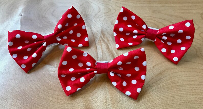 May include: Three red bow ties with white polka dots. The bow ties are made of fabric and have a simple design.