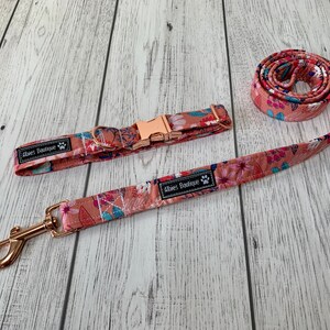 May include: A dog collar and leash set with a floral pattern in shades of peach, pink, and blue. The collar has a rose gold buckle, and the leash has a matching rose gold clasp. The set includes the text "Aloes Boutique".