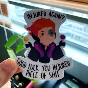 May include: A white sticker with a cartoon character with red hair and a black eye patch. The sticker has the text "INJURED AGAIN?" and "GOOD LUCK YOU INJURED PIECE OF SHIT" in black font. The character is wearing a purple and black outfit.