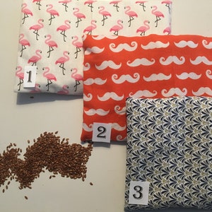 May include: Three fabric pouches with different patterns: pink flamingos, white mustaches on orange, and a geometric pattern in blue, green, and white. The pouches are numbered 1, 2, and 3. A pile of flax seeds is in the lower left corner.