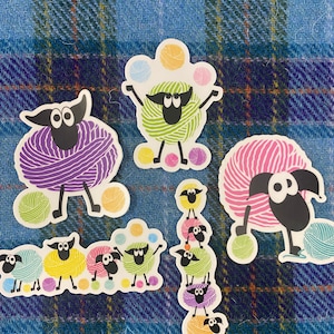 May include: A set of colorful yarn ball sheep stickers. The sheep are depicted in various poses, including juggling yarn balls, standing on top of each other, and holding yarn balls. The stickers are perfect for adding a touch of whimsy to any project.