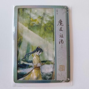 May include: A rectangular trading card featuring an illustration of a person in a yellow robe standing in a forest. The card has Japanese text and a holographic border. The background is a watercolor painting of a forest scene.