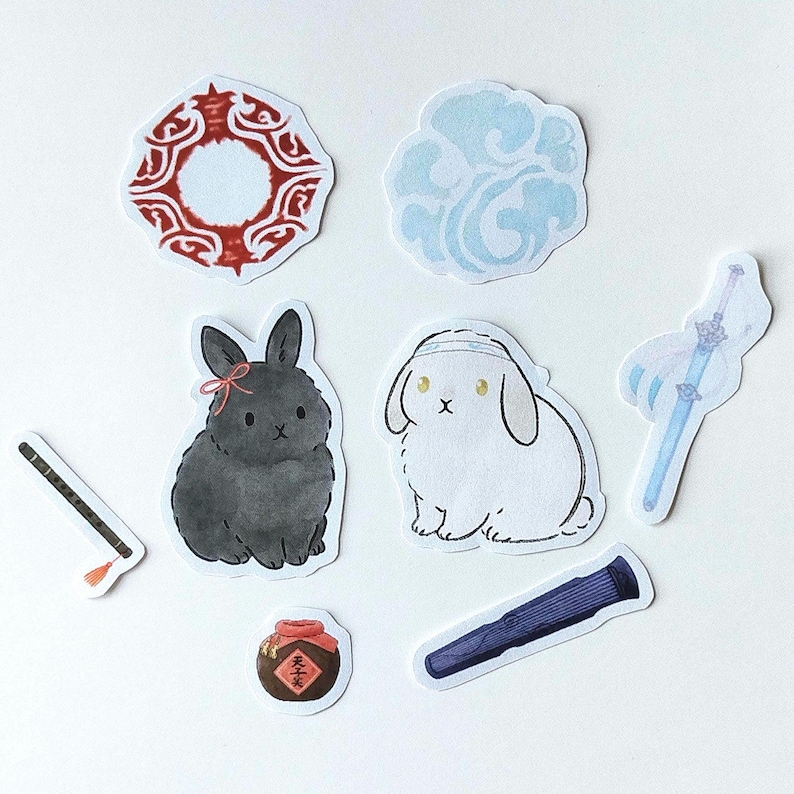 May include: A collection of die-cut stickers featuring various designs. Includes a black bunny with a pink bow, a white bunny, a blue sword, a red and white circular design, a blue cloud, a flute, a wine jar, and a dark blue tube.