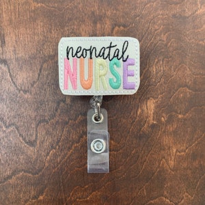 May include: A white rectangular badge with the text "neonatal NURSE" in rainbow colors. The badge is attached to a clear plastic retractable badge holder.