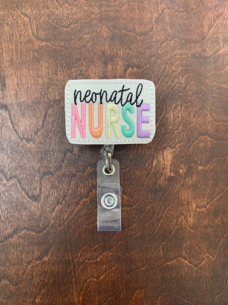 May include: A white rectangular badge with the text "neonatal NURSE" in rainbow colors. The badge is attached to a clear plastic retractable badge holder.