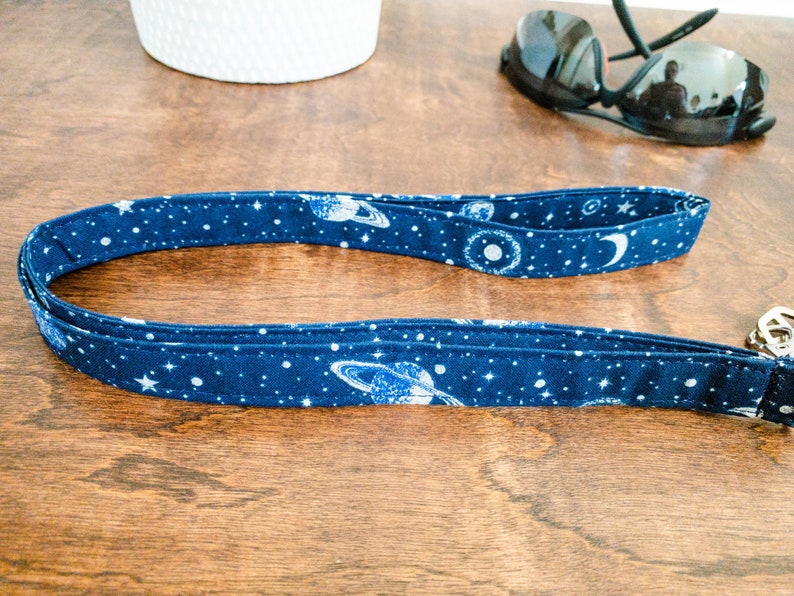 May include: A blue and white fabric key chain with a space theme. The key chain features planets, stars, and a crescent moon.