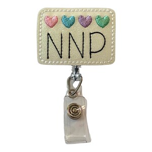 May include: A white rectangular badge holder with a white glitter background and a black embroidered NNP. The badge holder has a silver retractable badge reel with a clear plastic case and a gold metal clip. There are four embroidered hearts in pink, blue, purple, and green on the top of the badge holder.
