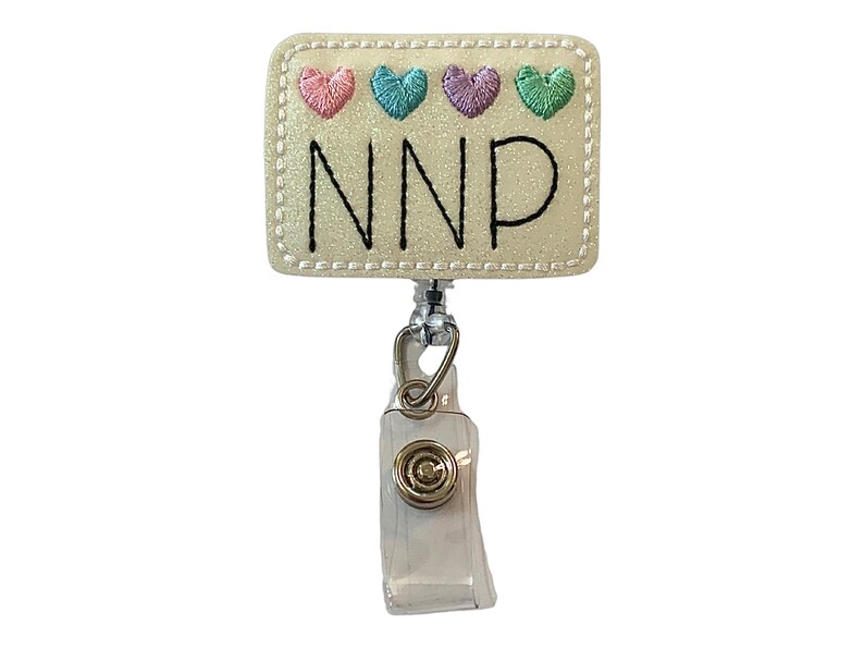May include: A white rectangular badge holder with a white glitter background and a black embroidered NNP. The badge holder has a silver retractable badge reel with a clear plastic case and a gold metal clip. There are four embroidered hearts in pink, blue, purple, and green on the top of the badge holder.