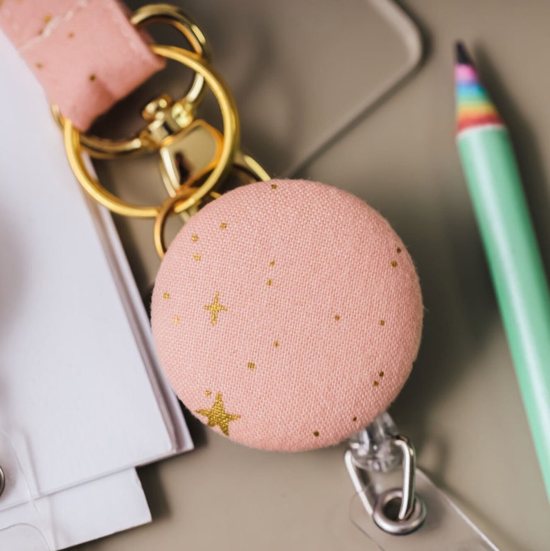 Pink fabric badge reel with gold stars. Hanging from lanyard on split keyring.