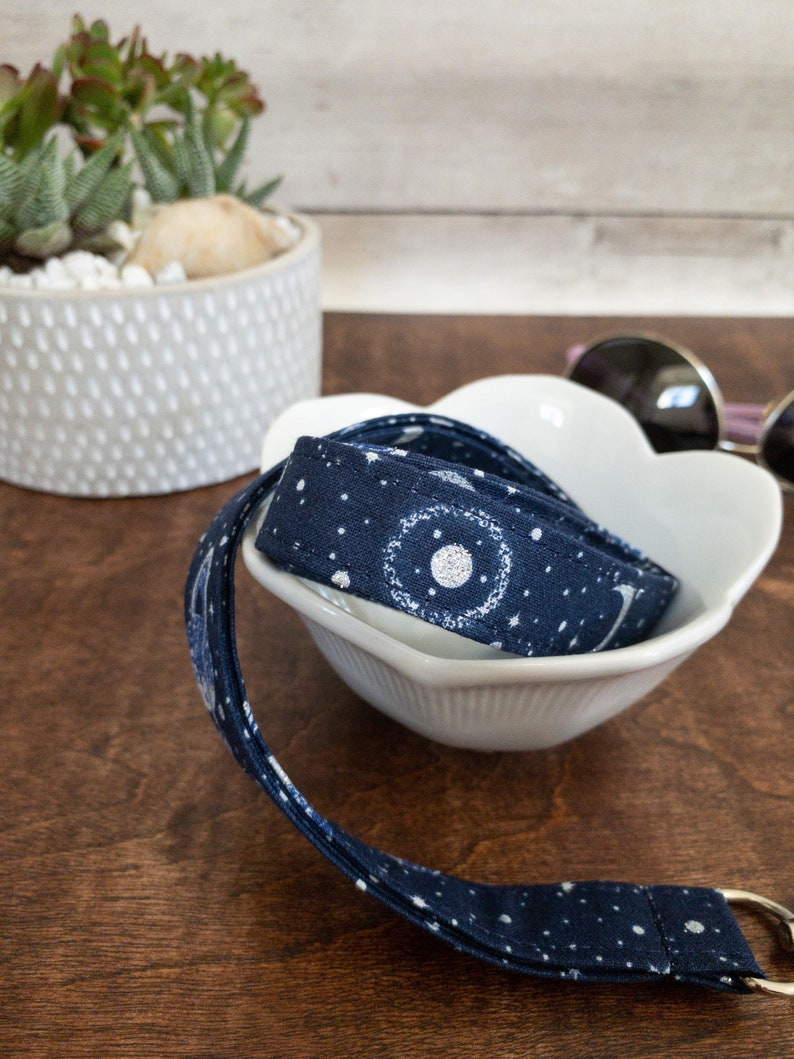 May include: A navy blue fabric lanyard with a white moon and stars pattern. The lanyard is coiled in a white ceramic bowl.
