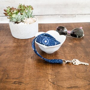 May include: A blue and white patterned lanyard with a silver key chain and a white bowl on a wooden surface.