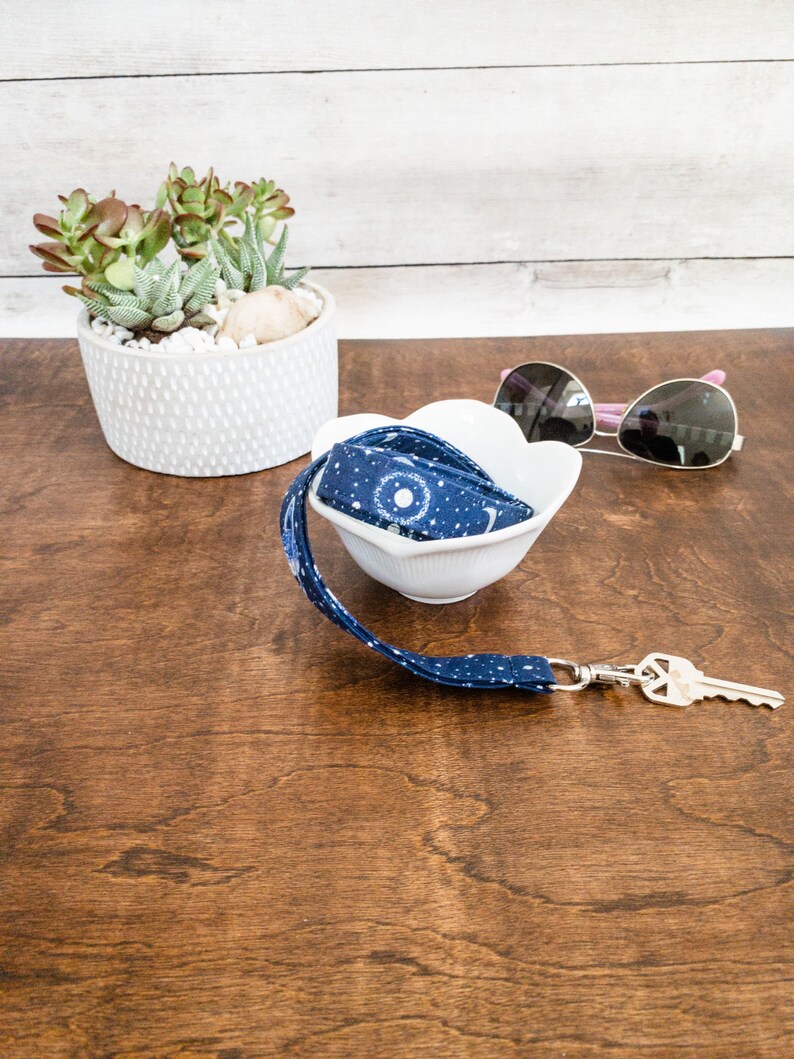 May include: A blue and white patterned lanyard with a silver key chain and a white bowl on a wooden surface.