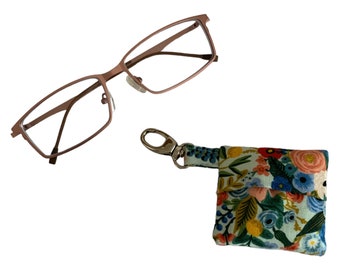May include: A pair of rectangular eyeglasses with a metallic copper-toned frame and a small square fabric pouch featuring a colorful floral pattern on a light blue background, equipped with a silver-toned metal lobster clasp for attachment.