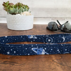 May include: A dark blue fabric leash with a white and silver print of planets, stars, and moons.