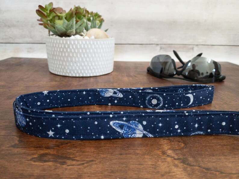 May include: A dark blue fabric leash with a white and silver print of planets, stars, and moons.