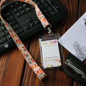 May include: A floral patterned lanyard with a clear plastic badge holder. The badge holder has a white card inside with the text "Hanging around you is awesome!" printed on it.