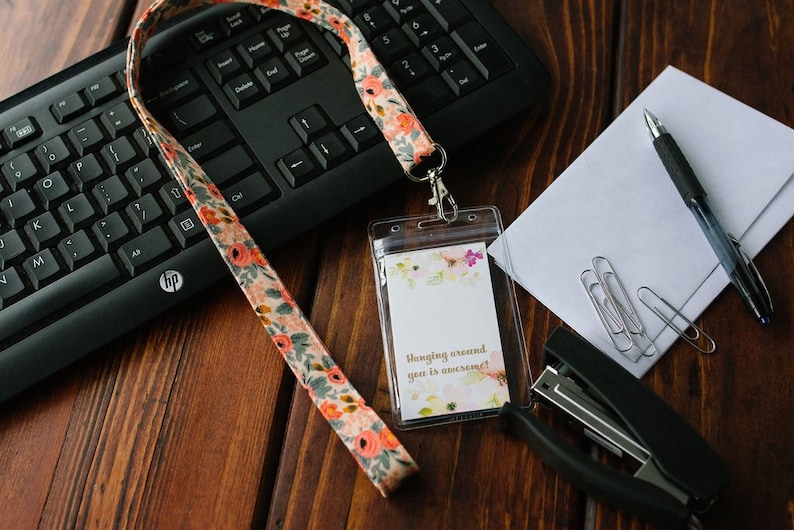 May include: A floral patterned lanyard with a clear plastic badge holder. The badge holder has a white card inside with the text "Hanging around you is awesome!" printed on it.