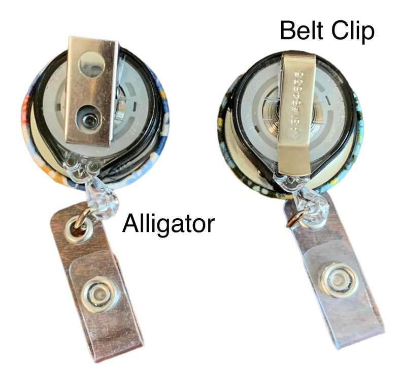 May include: A colourful fabric retractable badge holder with a metal alligator clip and a belt clip. The badge holder has a clear plastic strap and a brown wooden alligator clip.