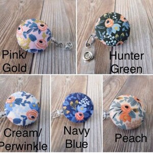 May include: Five different fabric covered buttons with floral patterns attached to retractable badge holders. The buttons are in the colors pink, hunter green, cream, navy blue, and peach.