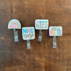 May include: Four white badge reels with embroidered designs and text. One has a rainbow and the text "NICU". Another says "NICU nurse" with baby feet. The third says "NICU" with hearts, and the last says "NICU nurse" in pastel colors.