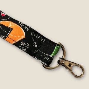 May include: Black lanyard with a white and green science-themed pattern. The lanyard has a silver swivel hook.