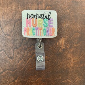 May include: White badge holder with a colorful embroidered design that reads "neonatal nurse practitioner".