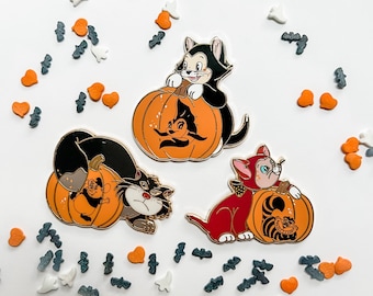 May include: Three enamel pins featuring Disney characters dressed as pumpkins. The pins are black, red, and orange with white accents. The characters are a cat, a dog, and a rabbit.