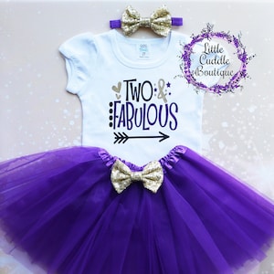 May include: Purple tulle tutu with a gold glitter bow, a white onesie with the text "Two & Fabulous" in black and purple, and a gold glitter headband with a bow.