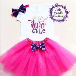 May include: A pink tulle tutu skirt with a purple sequined bow. A white t-shirt with the text "Miss Two Cute" in gold and purple glitter. A purple sequined headband with a bow.
