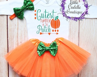 May include: Orange tulle skirt with a green sequin bow, a white long-sleeved onesie with the text "Cutest Pumpkin in the Patch" and a green sequin bow headband.