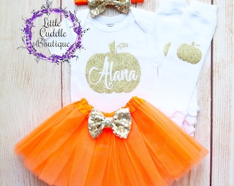 May include: Orange tulle tutu skirt with a gold glitter bow, a white bodysuit with a gold glitter pumpkin and the name "Alana" on it, a gold glitter headband with a bow, and white leg warmers with a gold glitter pumpkin.