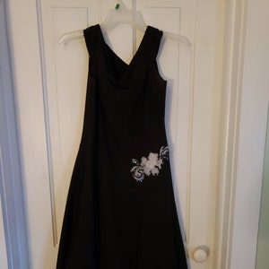 May include: A black sleeveless dress with a scoop neck and a floral embellishment on the side.