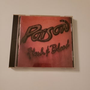 May include: A red CD case with a black spine. The front of the case features a black and white image of the band Poison with the text "Flesh & Blood".
