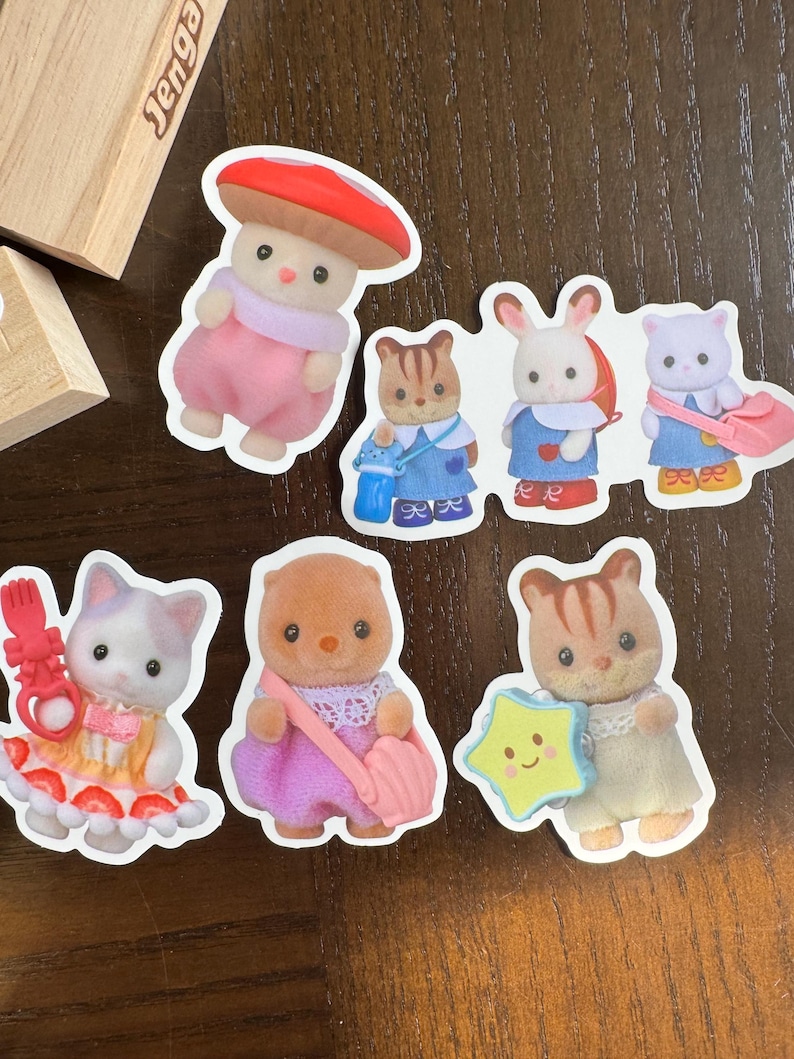 May include: A selection of colourful stickers depicting animal characters in various outfits. The stickers include a mushroom character, a cat in a strawberry dress, and other animal figures holding accessories like a star and a bag.
