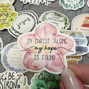 Może przedstawiać: Zbiór naklejek z inspirującymi cytatami i kwiatowymi wzorami. Jedna naklejka przedstawia różowy kwiat z napisem "IN CHRIST ALONE my hope IS FOUND". Inne naklejki zawierają frazy takie jak "Kind Words Are Like Honey" i "Jesus".