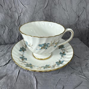 Puede incluir: Juego de taza y platillo blancos con borde dorado y diseño floral turquesa. La taza tiene un diseño acanalado y un asa dorada. El platillo tiene un patrón floral a juego y ribete dorado. Un juego de té clásico.