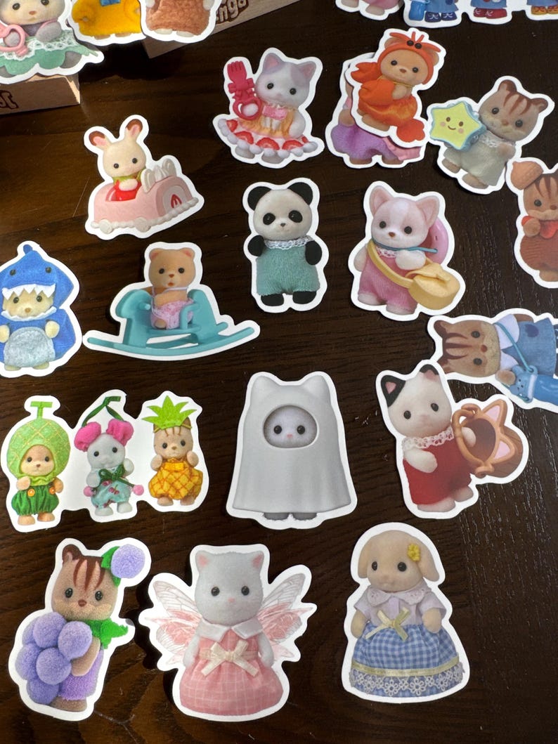 May include: A selection of colourful die-cut stickers showcasing animal characters in playful attire. The stickers include a panda, a bunny in a car, a bear on a rocking horse, and a cat in a dress. The stickers are on a brown surface.